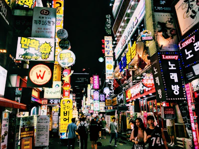 A bustling city street at night, glowing with neon signs and lively crowds.