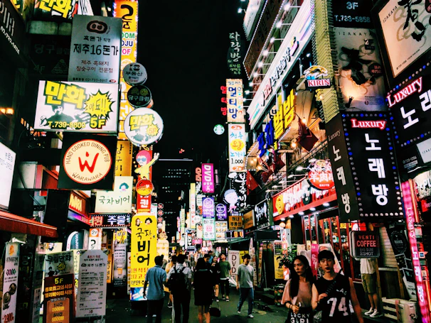 A bustling city street at night illuminated by colorful neon signs and lively crowds.