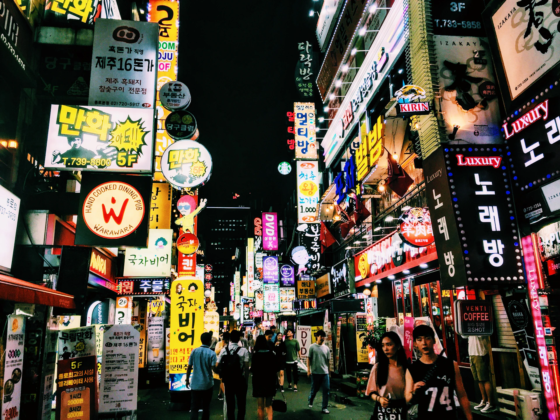 A bustling city street at night, illuminated by colorful neon signs and lively crowds.