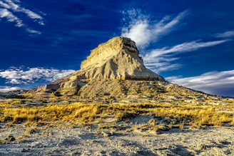 A sunlit mesa rising sharply against a clear blue sky, with rugged cliffs and sparse desert vegetation.