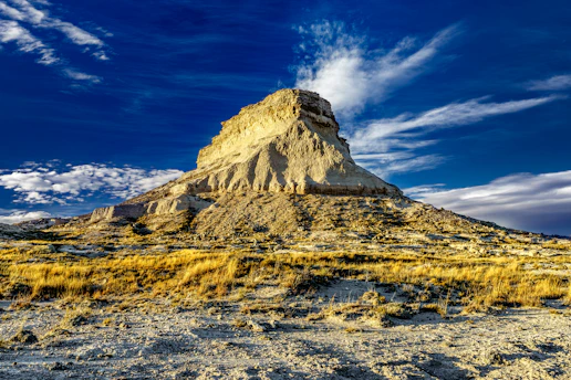 A sunlit mesa rising sharply against a clear blue sky, with rugged cliffs and sparse desert vegetation.