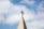 A church steeple with a red cross on top, set against a background of blue sky and white clouds.