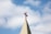 A church steeple with a red cross on top, set against a background of blue sky and white clouds.