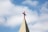A church steeple with a red cross on top, set against a background of blue sky and white clouds.
