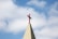 A church steeple with a red cross on top, set against a background of blue sky and white clouds.