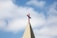 A church steeple with a red cross on top, set against a background of blue sky and white clouds.