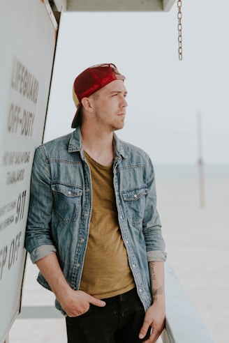man leaning on wall, in a denim jacket and 
