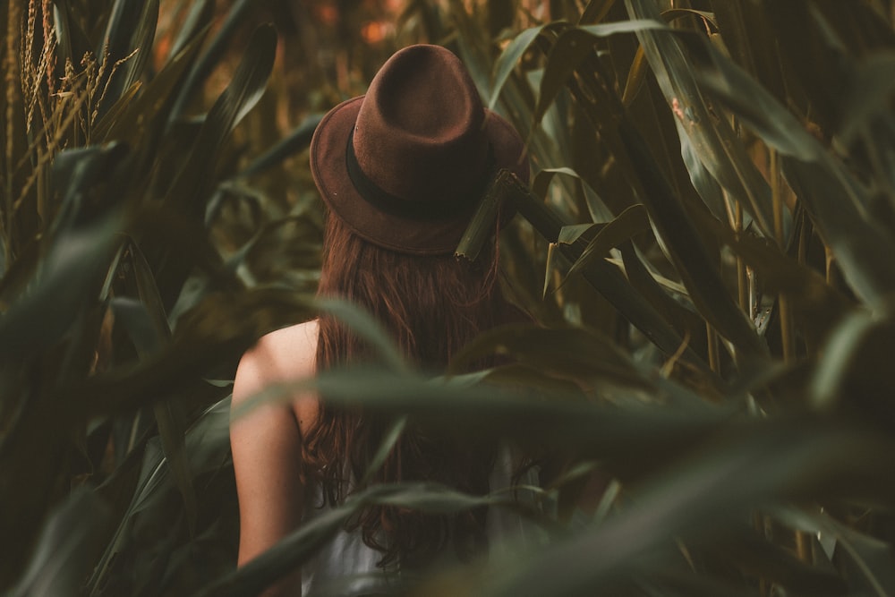 a woman wearing a hat standing in a corn field