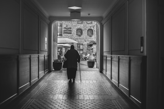 Photo showing a senior care worker assisting an elderly person with walking in a well-lit care facility.