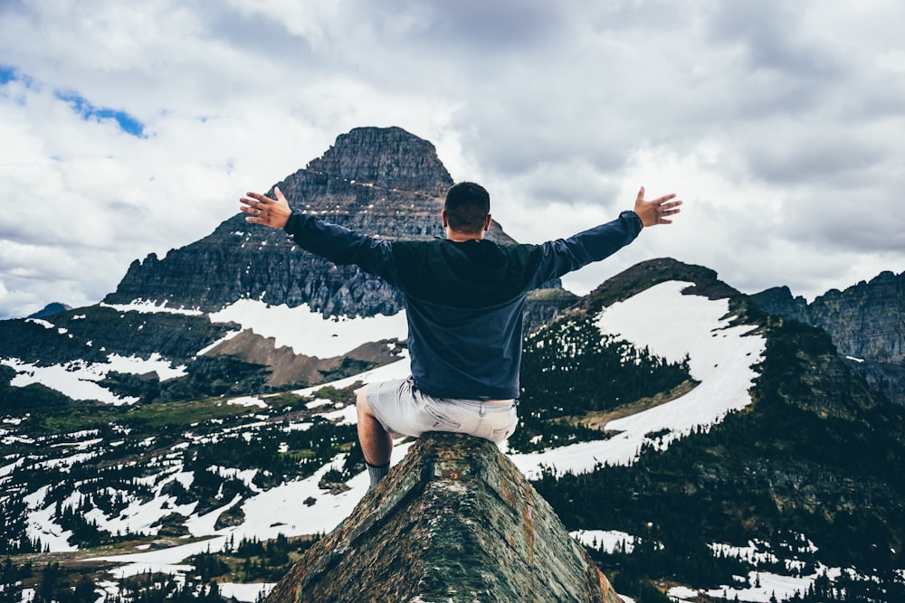 man sitting on cone rock spreading hands