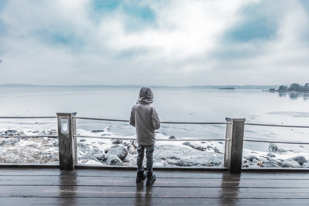 criança em pé em frente à costa na plataforma marrom