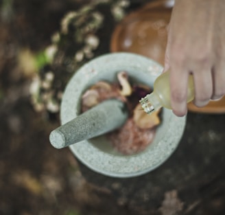 high angle photo of person pouring liquid from bottle inside mortar and pestle