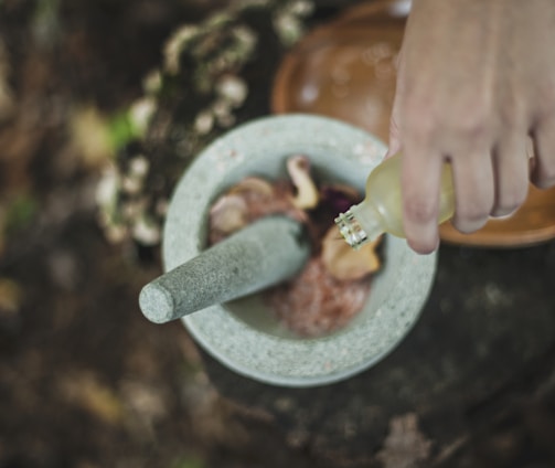 high angle photo of person pouring liquid from bottle inside mortar and pestle