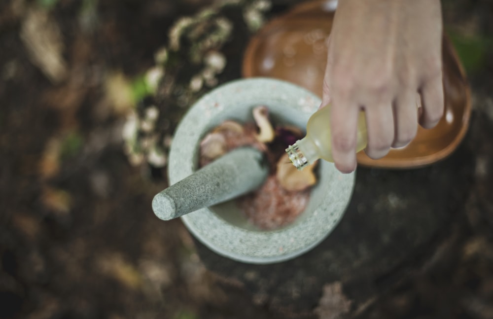 Photo en plongée d’une personne versant du liquide d’une bouteille à l’intérieur d’un mortier et d’un pilon