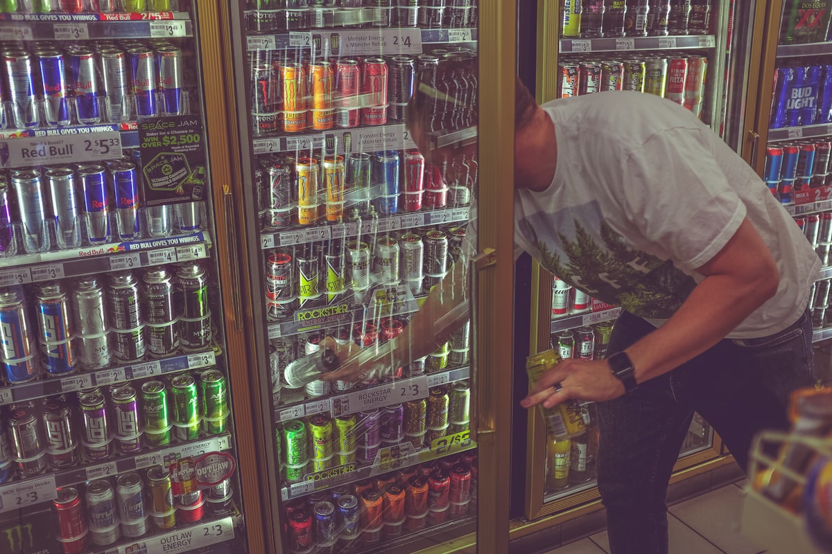 Person reaching for a beverage can in a convenience store cooler