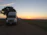 A weathered semi truck parked beside a quiet country road at sunset.