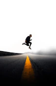 man jumping above gray and yellow concrete road at daytime