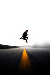 man jumping above gray and yellow concrete road at daytime
