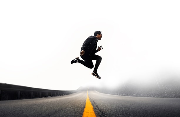 man jumping above gray and yellow concrete road at daytime