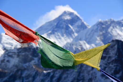 Colorful prayer flags flutter against a backdrop of snow-covered mountains, with a clear blue sky above.