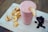 A creamy pink smoothie fills a glass, garnished with a dried apple slice. On a wooden board beside it, there are additional dried apple slices and a small pile of dark dried fruits, possibly berries.