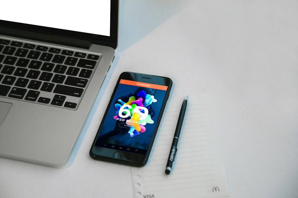 A smartphone next to a pen and laptop.