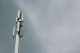 A tall telecommunications tower with several antenna panels and a cloudy sky background.