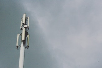 A tall telecommunications tower with several antenna panels and a cloudy sky background.