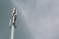A tall telecommunications tower with several antenna panels and a cloudy sky background.