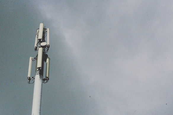 A tall telecommunications tower with several antenna panels and a cloudy sky background.