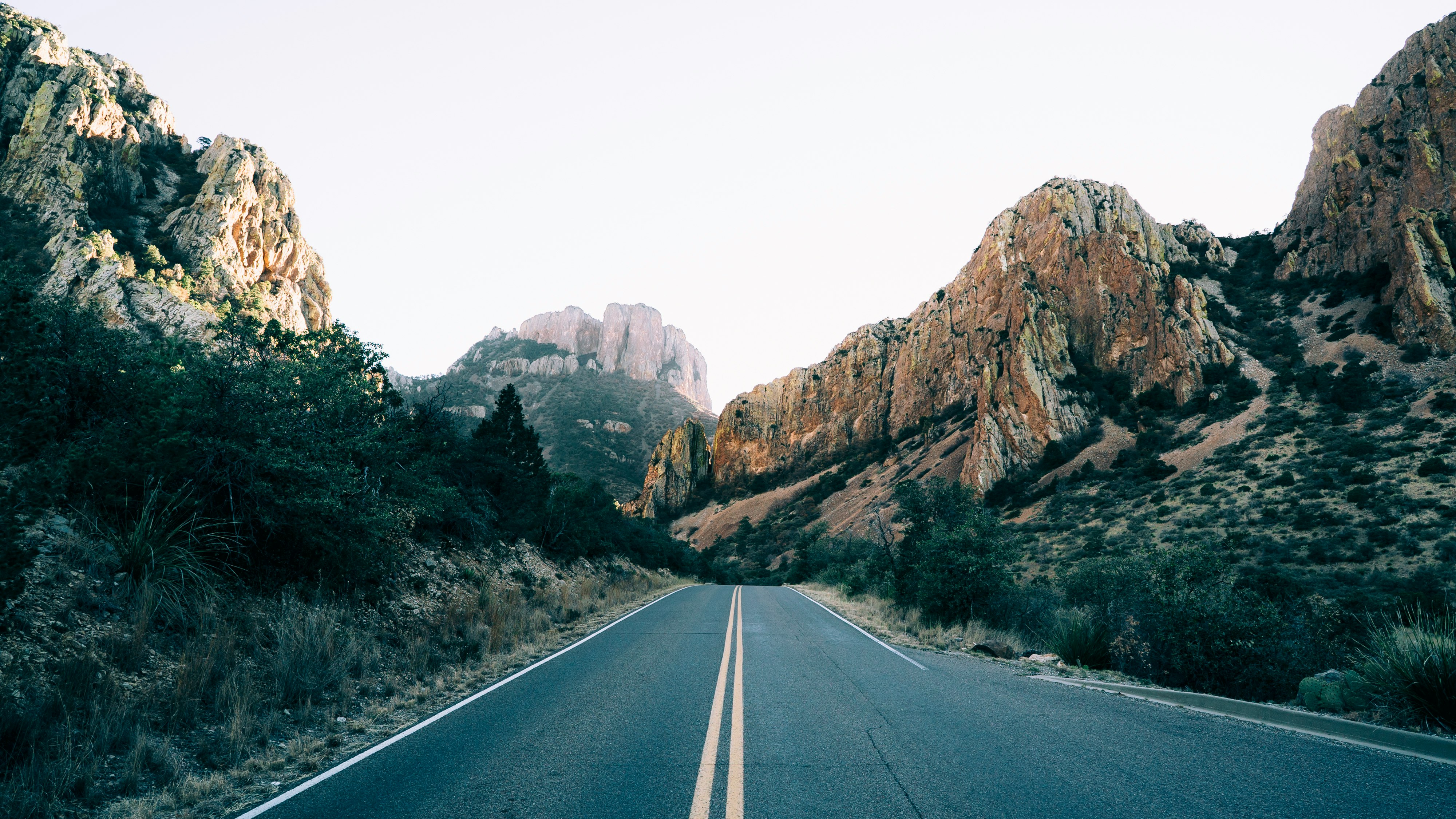 road lined with rocky mountain at daytime