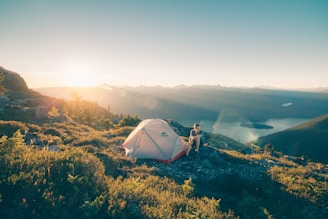 man sitting on stone beside white camping tent