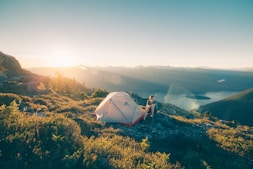 man sitting on stone beside white camping tent