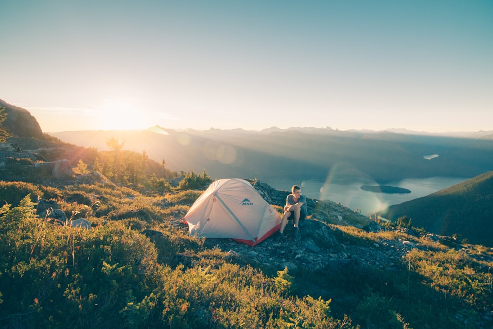 man sitting on stone beside white camping tent