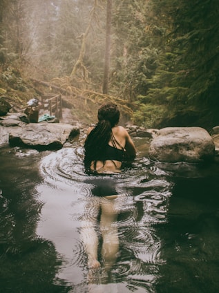 A traveler enjoying a serene hot spring surrounded by lush greenery at sunset.