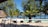 A serene beach setting with a tranquil pool surrounded by lounge chairs. Palm trees and lush greenery provide shade, while the ocean stretches out in the background. Straw-roofed structures add to the tropical atmosphere.