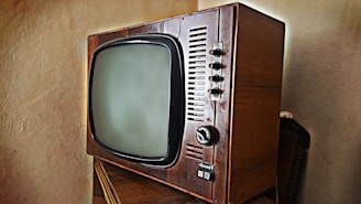 A vintage television set with a wooden frame and a rounded screen is displayed. The television features several knobs and buttons on the right side for manual adjustments. The design is reminiscent of mid-20th century electronics, highlighting its retro aesthetic.