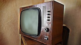 A vintage television set with a wooden frame and a rounded screen is displayed. The television features several knobs and buttons on the right side for manual adjustments. The design is reminiscent of mid-20th century electronics, highlighting its retro aesthetic.