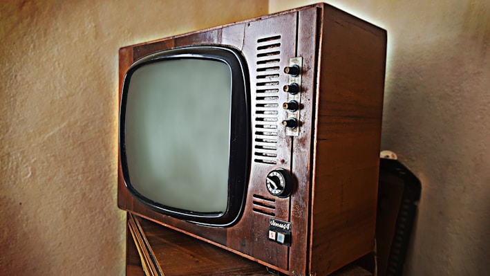 A vintage television set with a wooden frame and a rounded screen is displayed. The television features several knobs and buttons on the right side for manual adjustments. The design is reminiscent of mid-20th century electronics, highlighting its retro aesthetic.