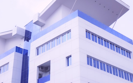 A modern building with a minimalist design, characterized by its white and blue facade. The structure includes large windows and geometric forms, with an emphasis on clean lines and symmetry.