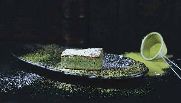 A chef sprinkling culinary grade matcha powder over freshly baked matcha-flavored pastries.