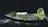 A slice of green tea cake sits on a dark plate, dusted with powdered sugar and surrounded by a sprinkle of matcha powder. In the background, a sieve is seen tipped over with some of the matcha powder spilled onto the surface.