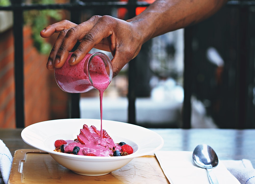 person pouring pink liquid on fruits