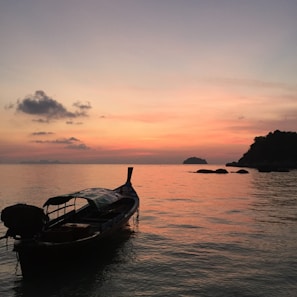A serene sunset over the turquoise waters of Krabi beach with traditional long-tail boats.