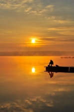 A serene fishing scene with a boat on calm waters at sunrise.
