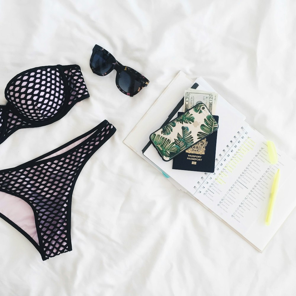 A flatlay with a notebook, a phone, a passport, sunglasses and a bikini