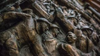 An intricately carved relief featuring several human figures with a dynamic composition, likely depicting a historical or artistic scene. The material appears to be a dark stone or bronze, with shadows accentuating the depth and details of the carving.