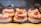 A display of pastries arranged neatly in rows, each topped with powdered sugar, cream, strawberries, and pastry crust. The desserts are placed in a well-lit setting with a warm and inviting atmosphere.