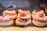 A display of pastries arranged neatly in rows, each topped with powdered sugar, cream, strawberries, and pastry crust. The desserts are placed in a well-lit setting with a warm and inviting atmosphere.