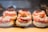 A display of pastries arranged neatly in rows, each topped with powdered sugar, cream, strawberries, and pastry crust. The desserts are placed in a well-lit setting with a warm and inviting atmosphere.